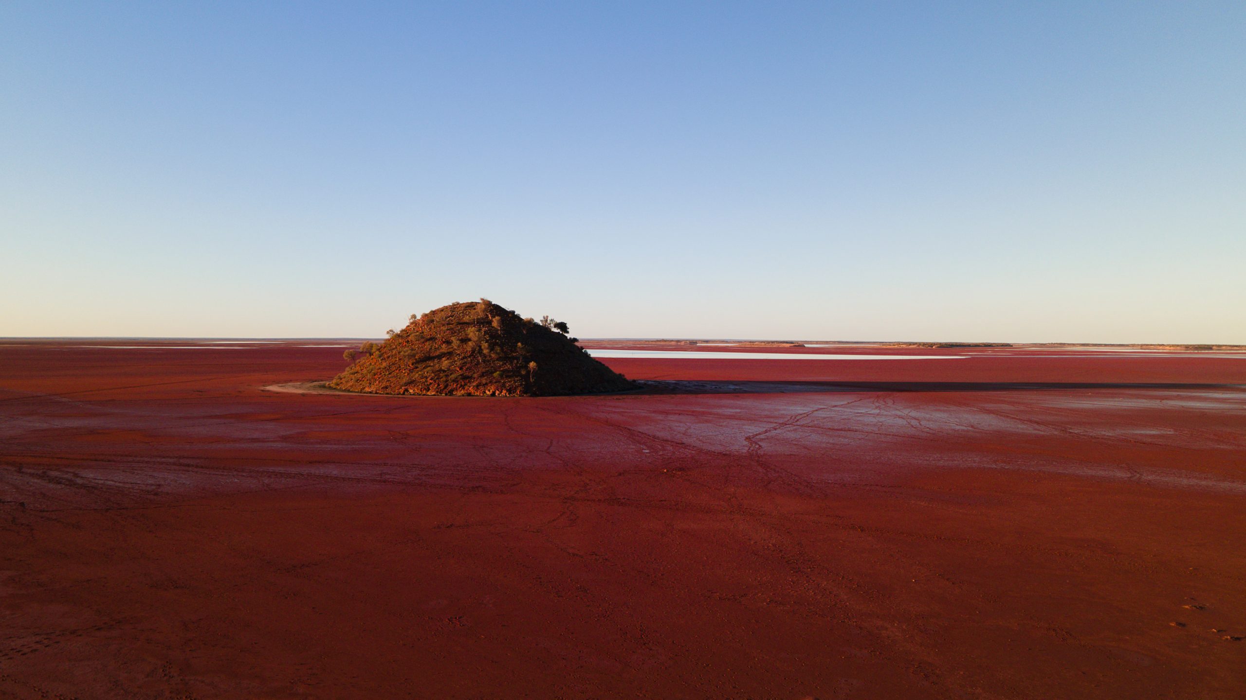 Sunset at Lake Ballard in Western Australia, with the Seven Sisters hills in view, casting long shadows across the red mud flats of the remote desert landscape