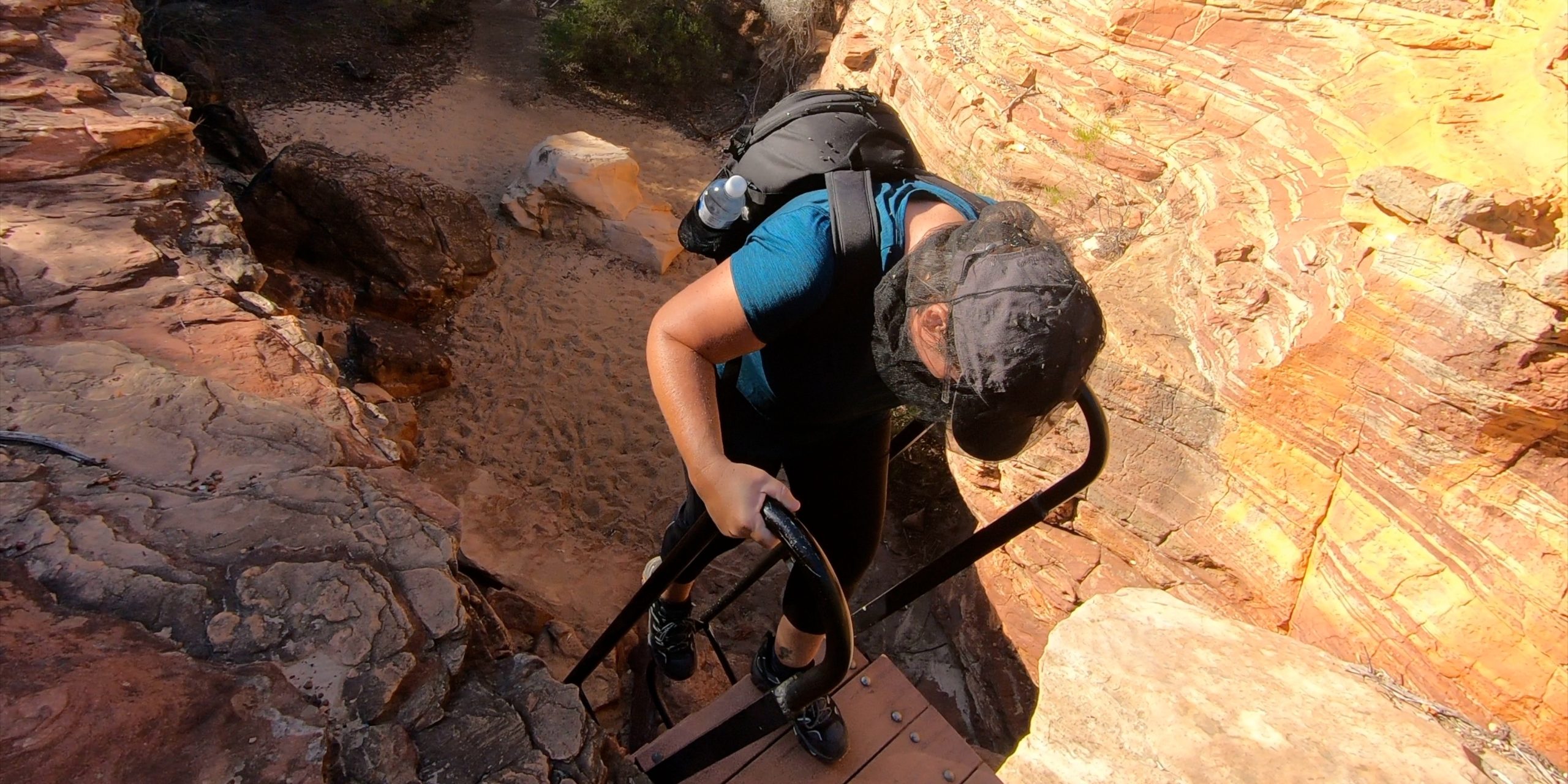 Female hiker descending a metal ladder on the Z Bend River Trail in Kalbarri National Park, Western Australia,highlighting the rugged terrain and challenging trail conditions