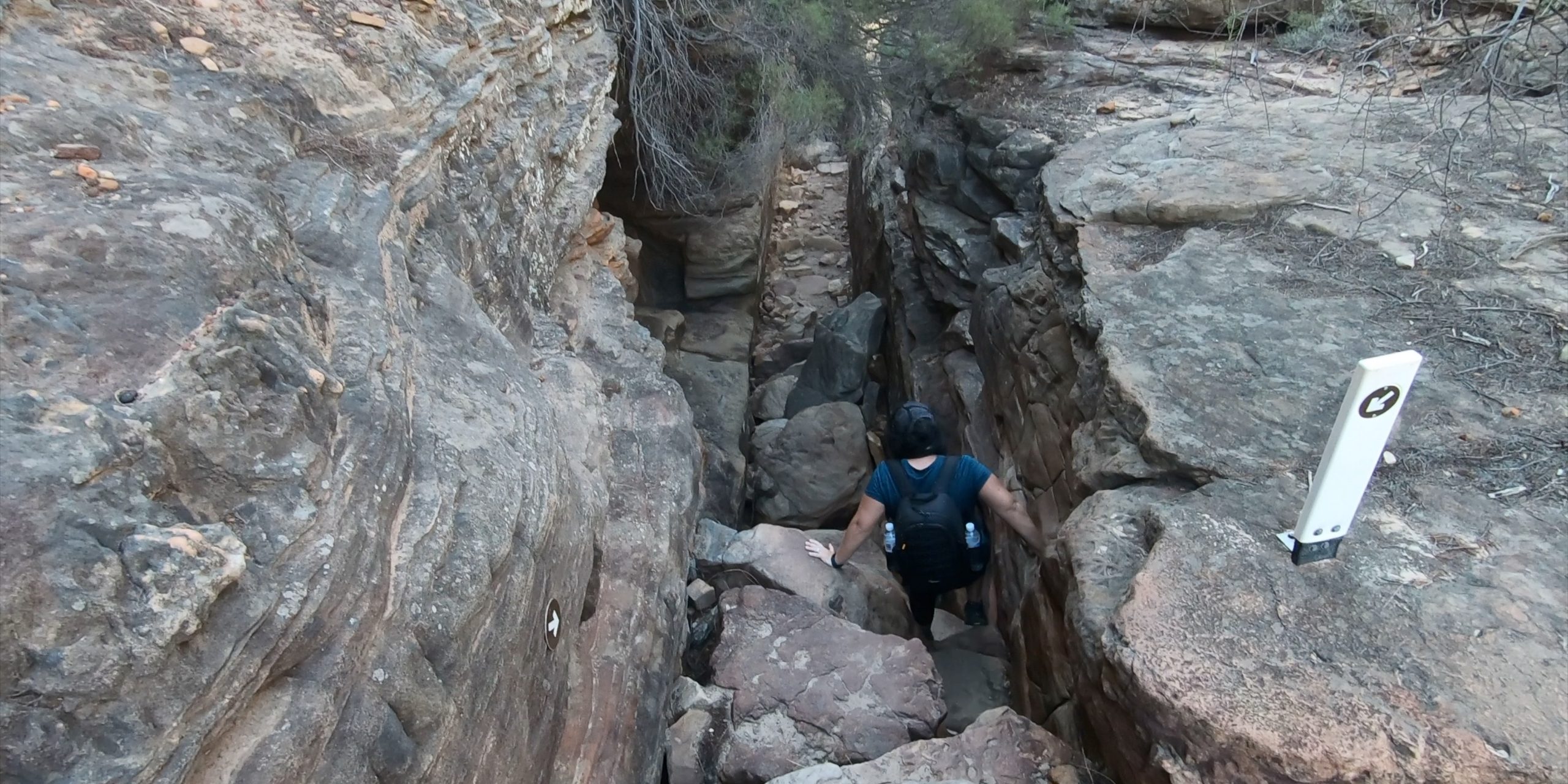 Female hiker navigating large rocky boulders along the Z Bend River Trail in Kalbarri National Park, Western Australia
