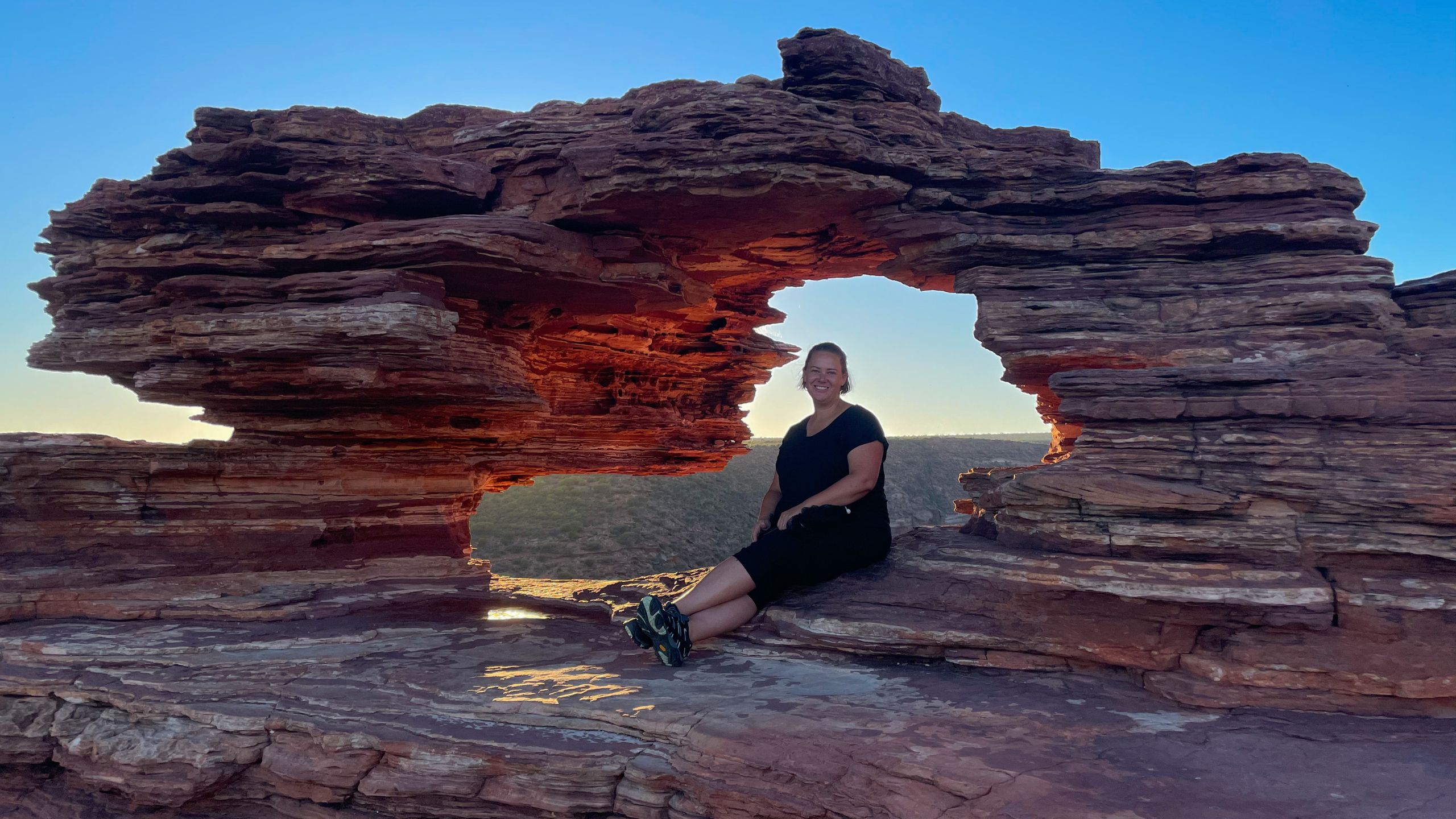 Woman sitting in Nature's Window with the sun glow lighting up the red sandstone.