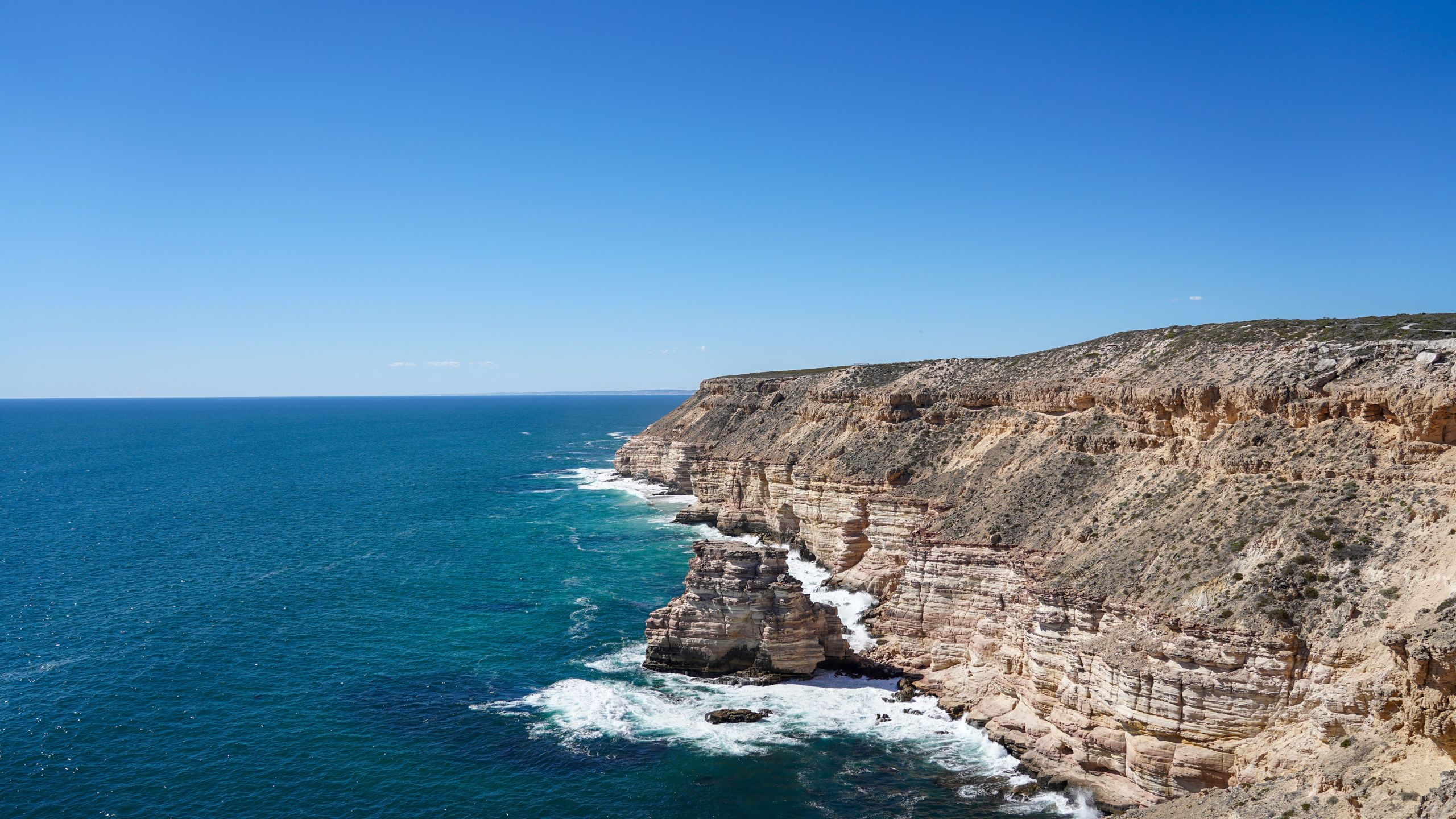 Daytime view of Kalbarri’s coastal cliffs in Western Australia, showcasing Island Rock sea stack, striking sandstone formations, and the vibrant blue waters of the Indian Ocean under a bright blue sky