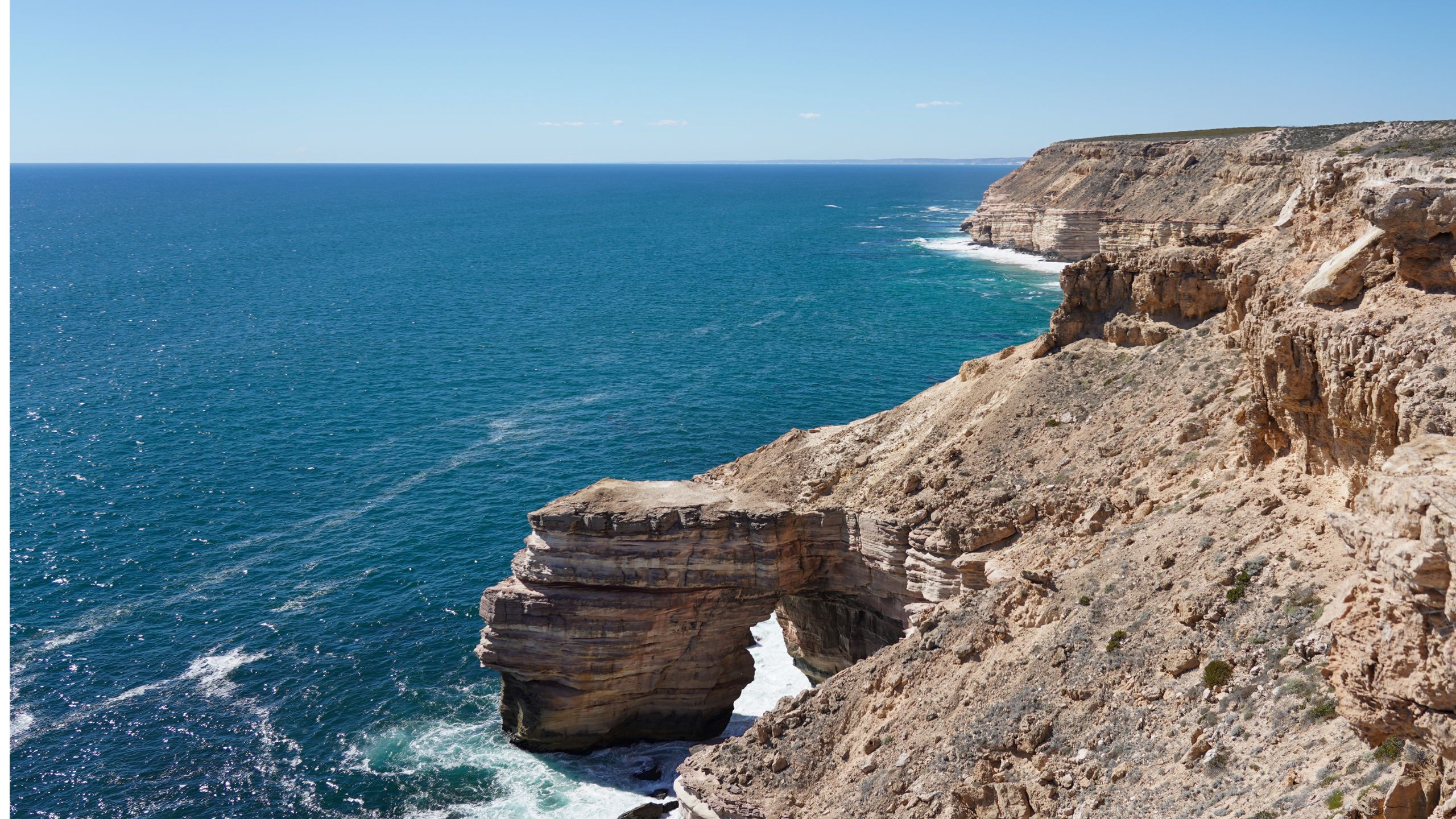 Daytime view of Natural Bridge in Kalbarri National Park, Western Australia, featuring the dramatic coastal rock arch formation above the Indian Ocean, with clear blue skies and rugged sandstone cliffs