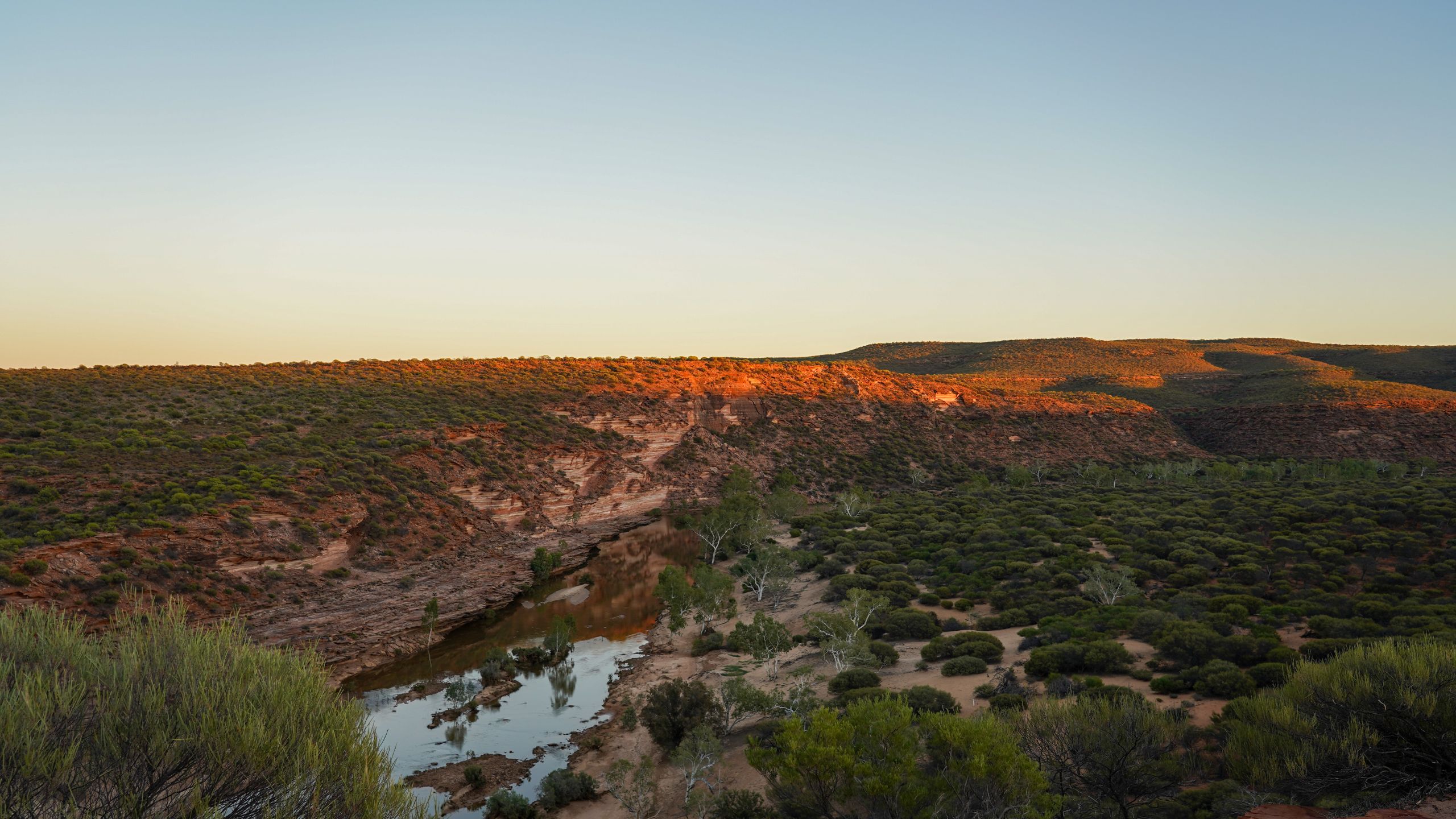 Sunrise casting an orange glow over the Murchison Gorge in Kalbarri National Park, Western Australia, illuminating the rugged red cliffs and winding river below