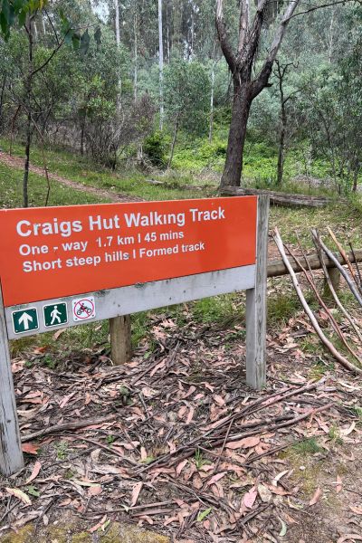 Start of the Craig’s Hut walking track with trail sign and walking sticks resting nearby, set in Victoria’s Alpine National Park.
