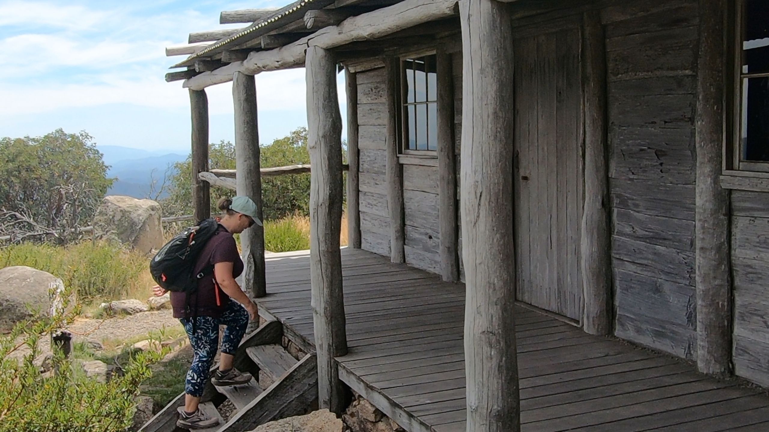 Woman climbing the wooden steps of Craig’s Hut with panoramic alpine views in the background, located in Victoria’s High Country.