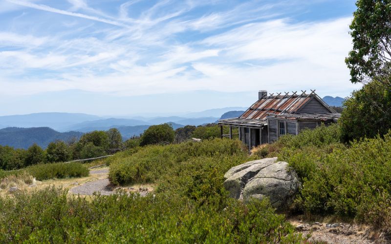 Craig’s Hut on a sunny day with scattered clouds, set against the scenic backdrop of the Victorian High Country.