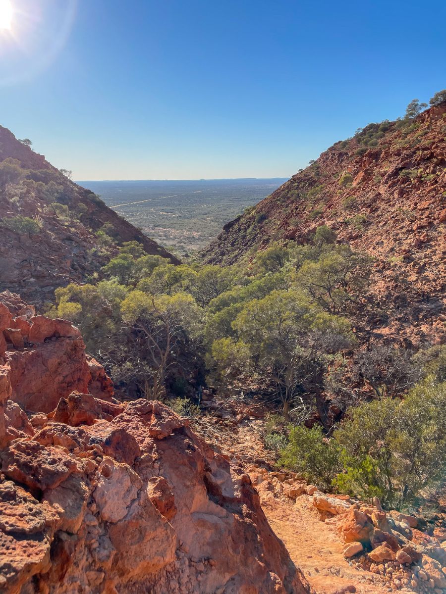View looking back toward the plains from the Kennedy Range Escarpment Trail after climbing up the rocky slope, showing the rugged terrain and wide open outback landscape.