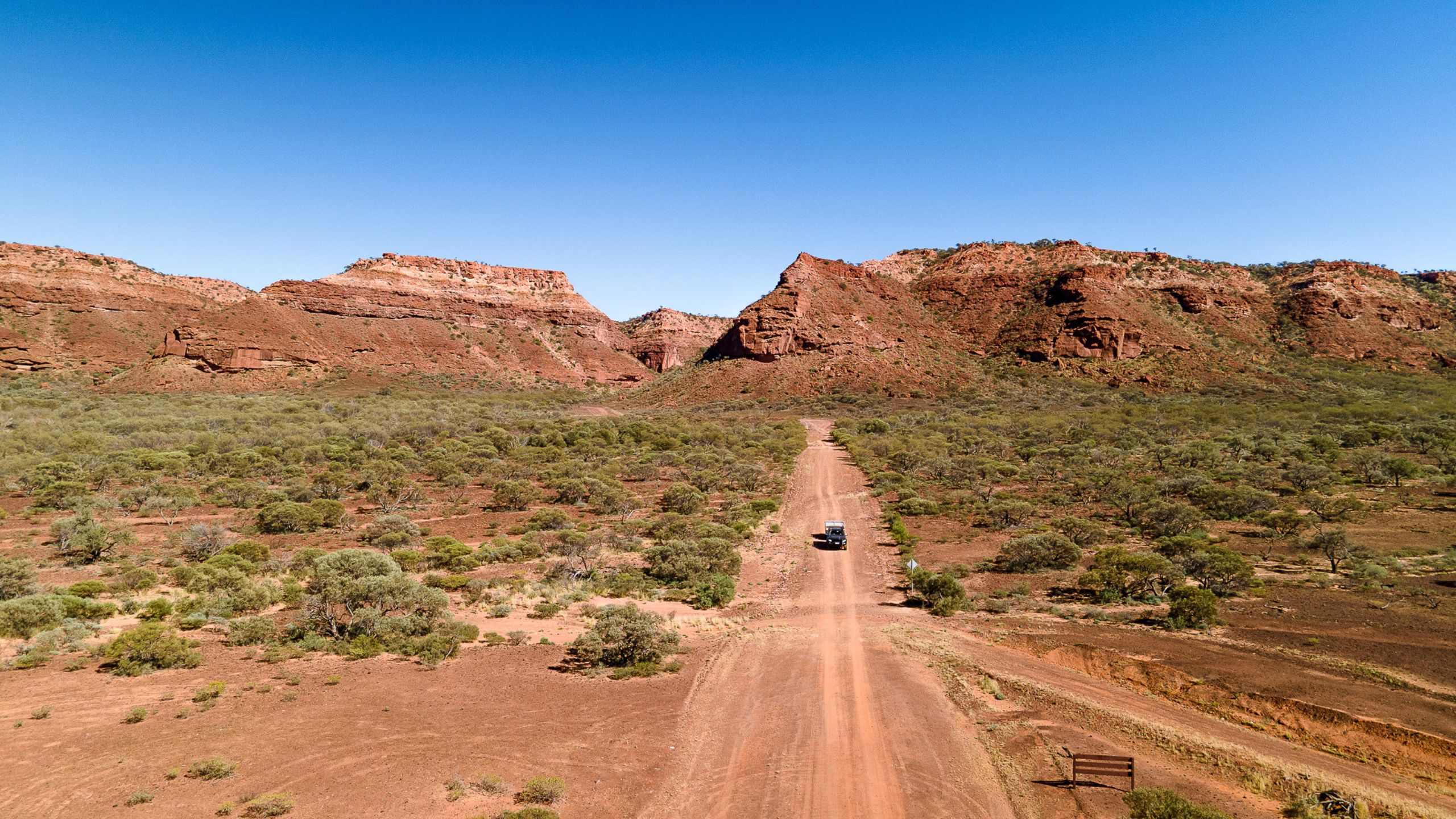 A car and camper on red dirt unsealed road with the Kennedy Range, WA in the background. Remote outback WA road trip.