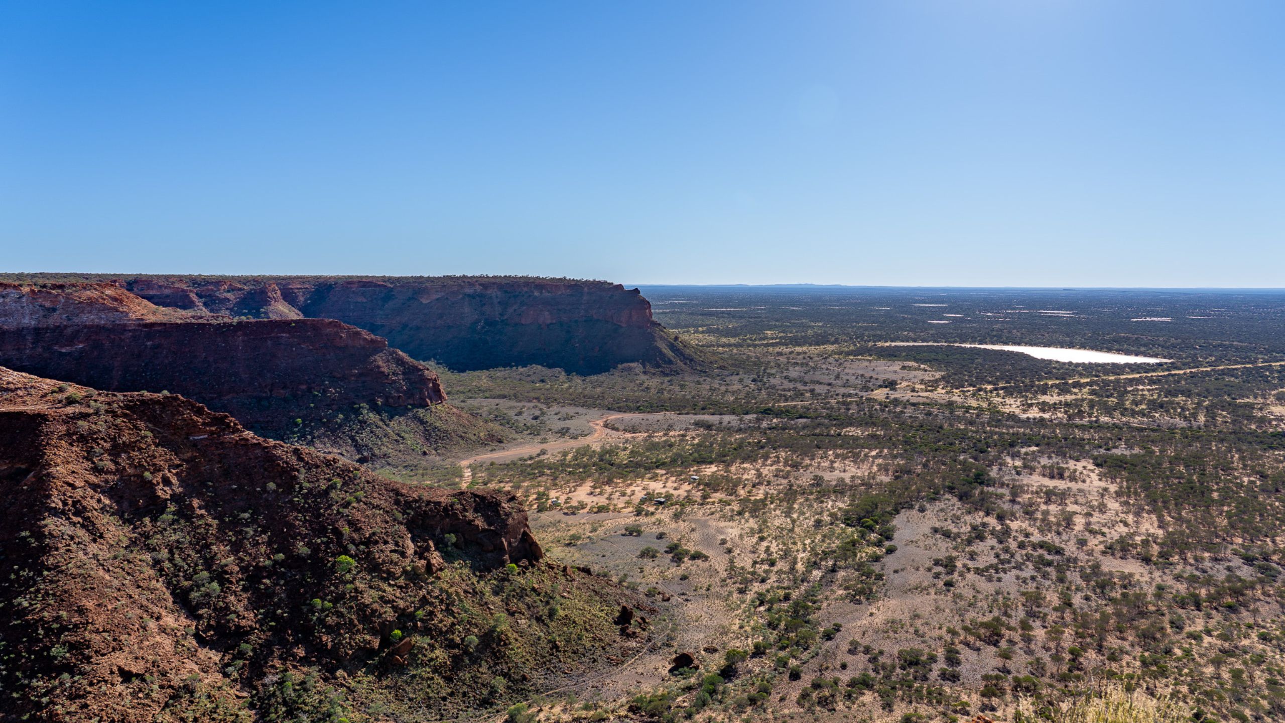Panoramic view of the Kennedy Range National Park from the plateau overlooking Temple Gorge Campground in Western Australia, showcasing rugged red cliffs, desert landscape, and clear blue sky.
